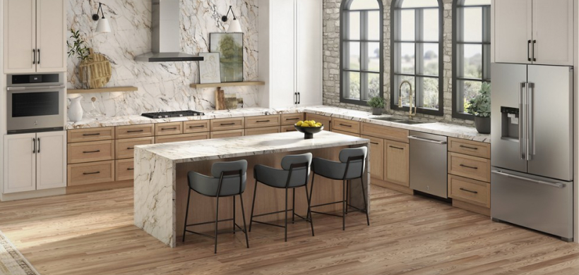 A kitchen with an island with three chairs, a JennAir wall oven, JennAir dishwasher, JennAir cooktop and JennAir French Door Refrigerator. On the counters are potted plants and a vase.